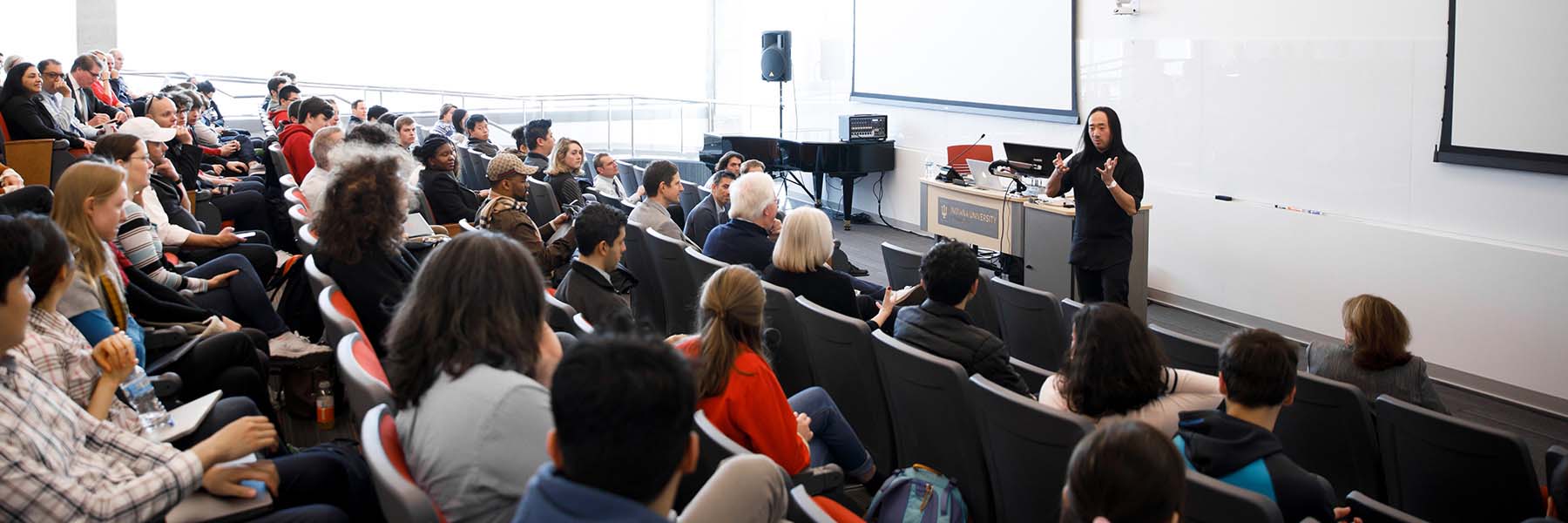 Students and professionals sit and listen to a speaker in a large lecture hall.