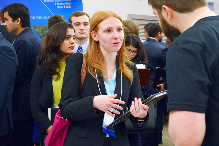 A student holds a portfolio and speaks with an employer at a career fair.